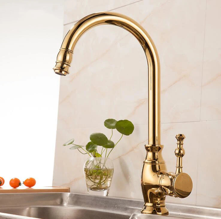 Gold kitchen faucet with a plant in a glass vase on a countertop.
