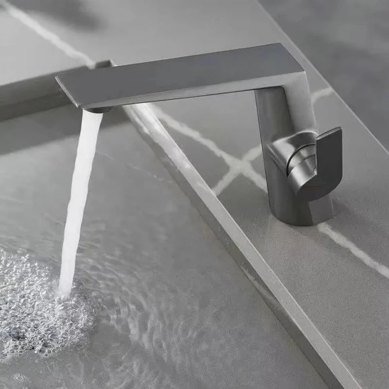 Modern silver faucet with water flowing into a bathtub.