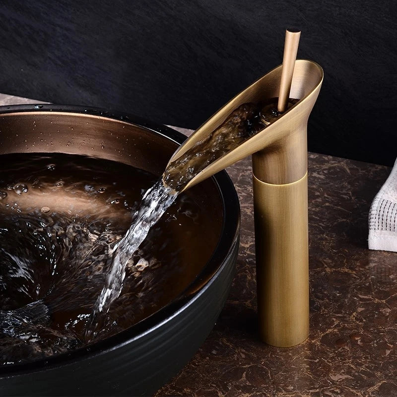 Gold faucet pouring water into a black basin on a dark marble surface.